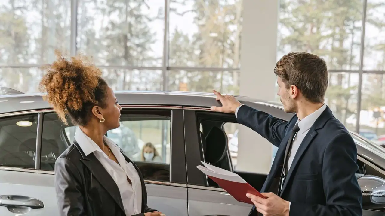 car dealership showroom with salesperson presenting a vehicle to a customer